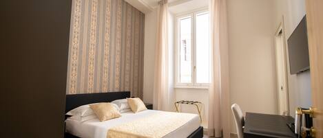 Una habitación de hotel con cama, escritorio, silla, televisión y ventana con cortinas.