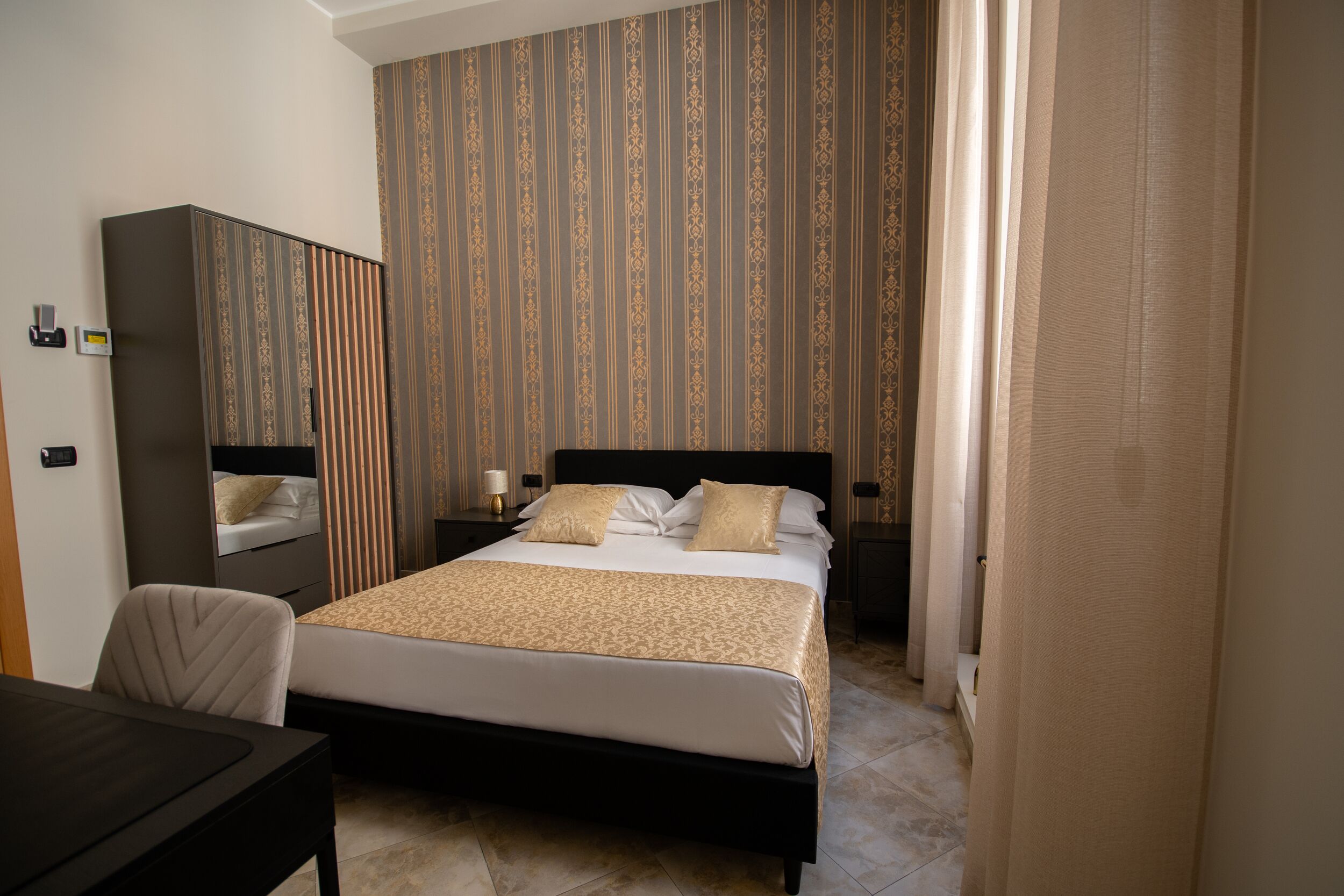 A hotel room with a bed, a desk, a wardrobe, and a mirror.