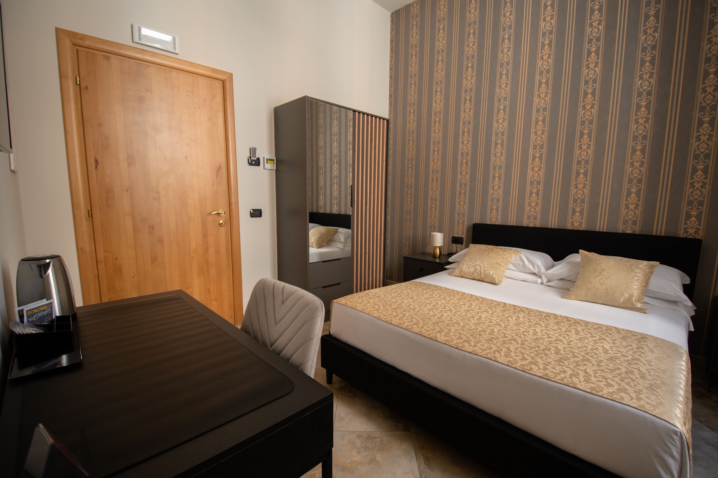 A hotel room with a bed, a desk, a wardrobe, and a coffee maker.