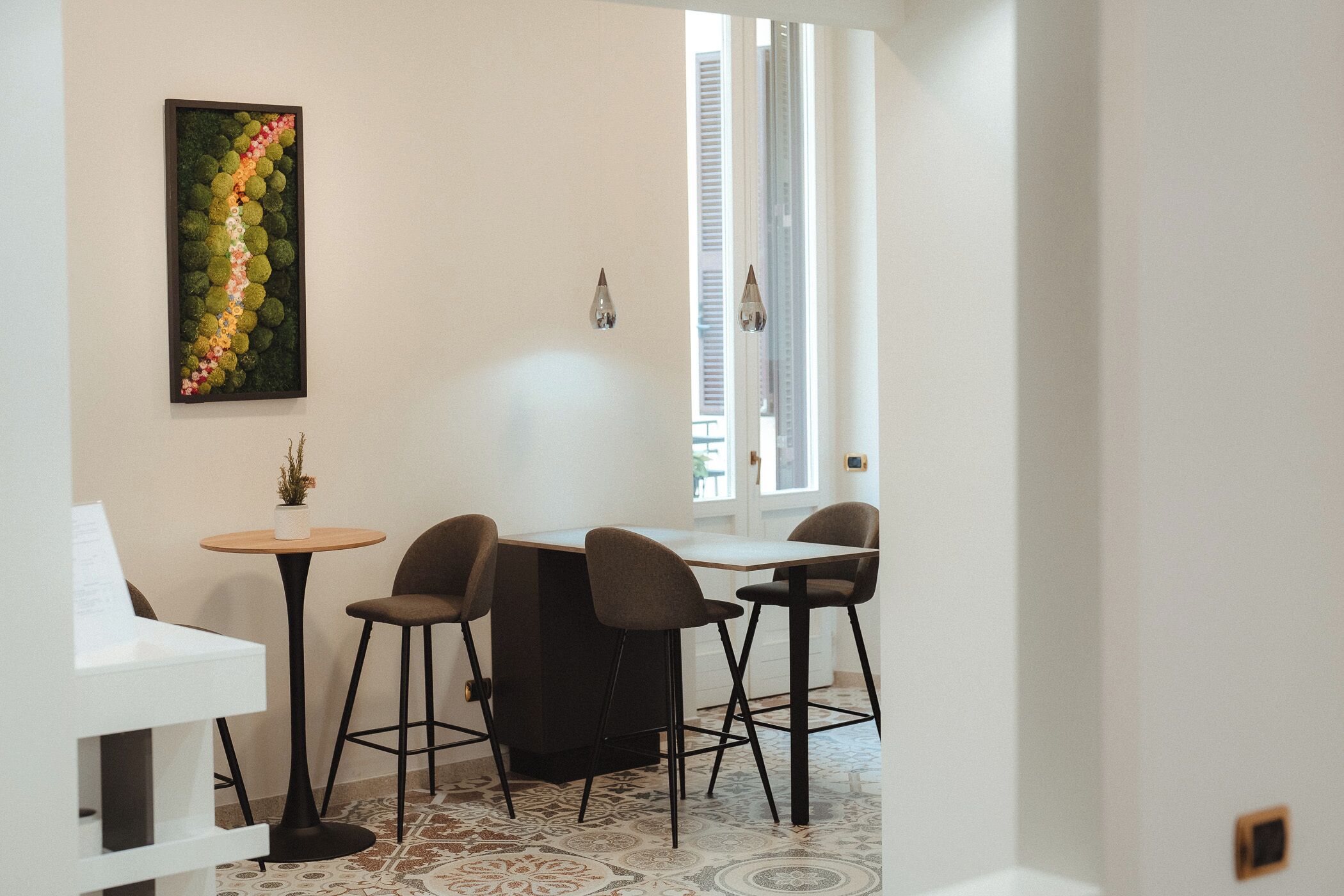 Una cocina moderna con comedor, que incluye una isla central con taburetes de bar, una pequeña mesa redonda con una planta y un elemento decorativo en la pared.