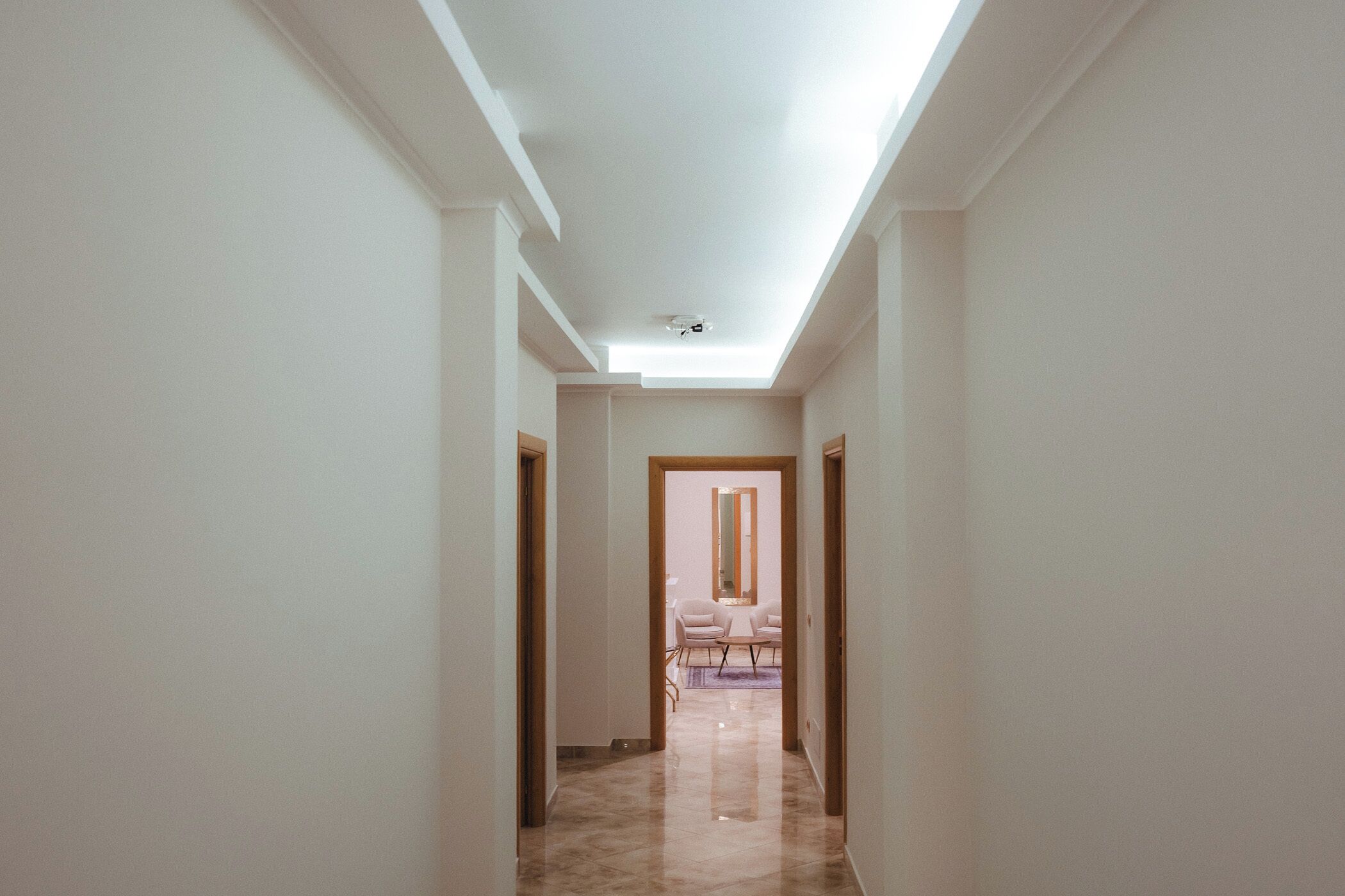 A hallway with a ceiling light, a door leading to a dining area with a table and chairs, and a marble floor.