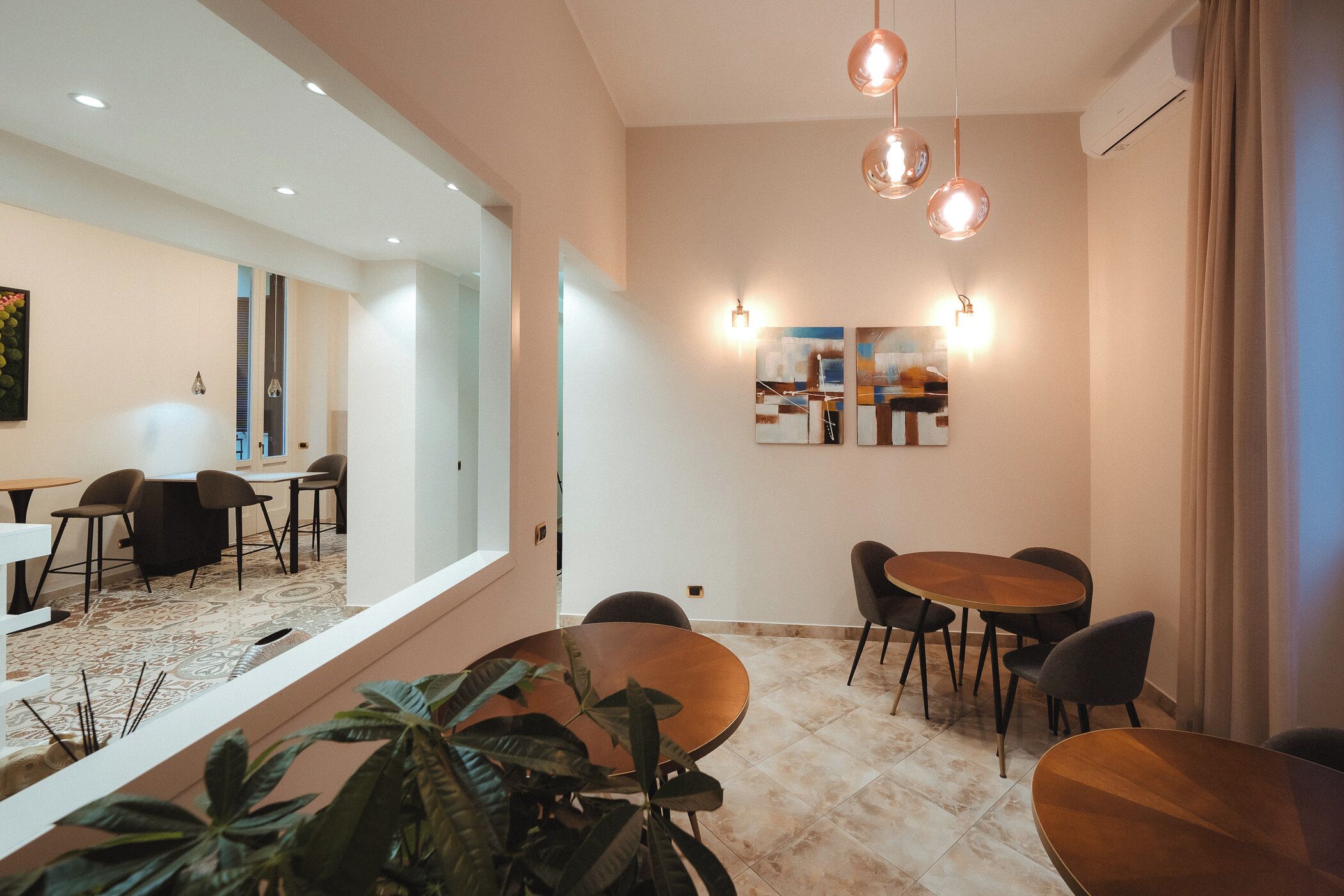 A modern dining area with round wooden tables and chairs, a large mirror, and wall-mounted artwork.