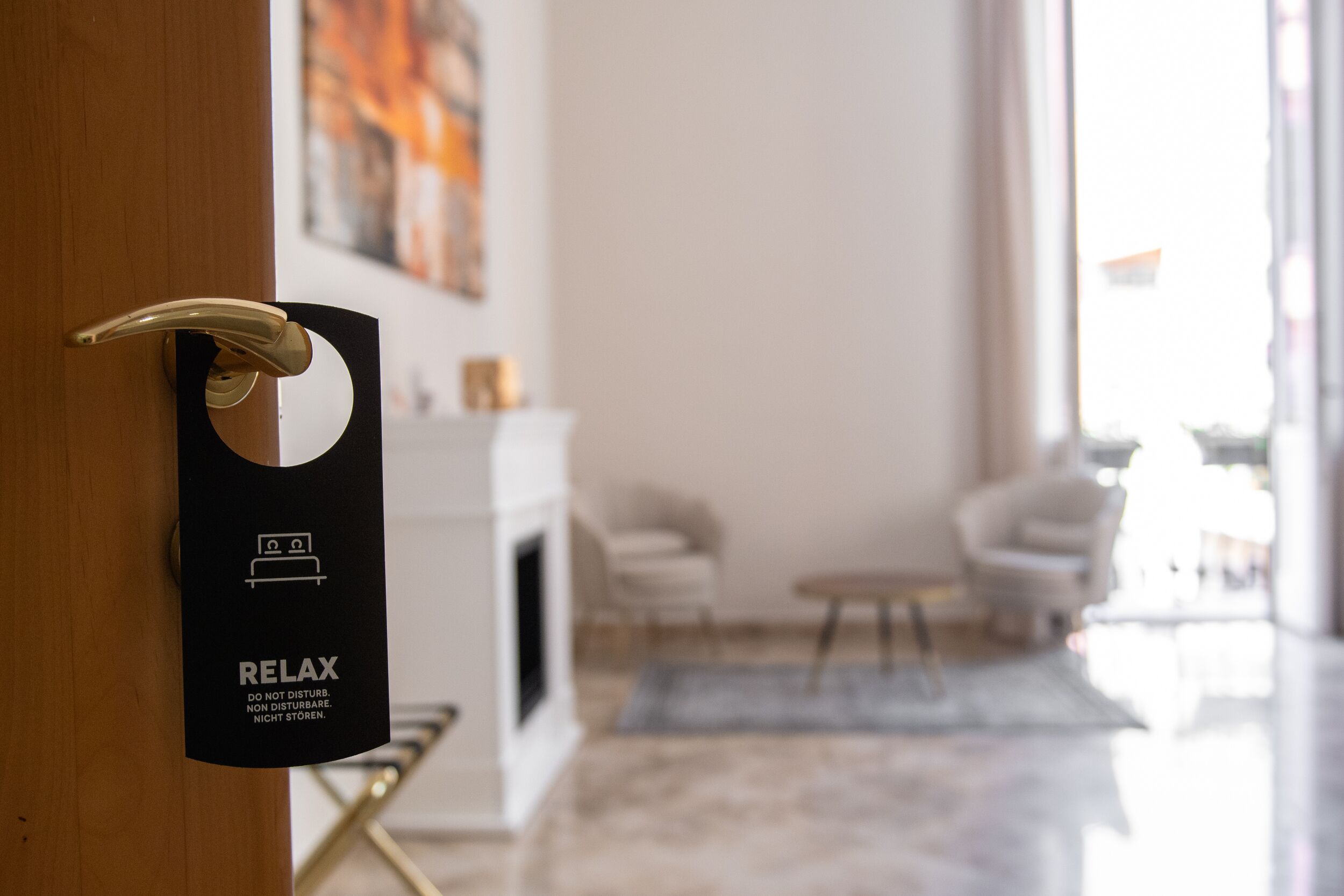 A hotel room door with a 'RELAX' sign, a white fireplace, and a modern living area with a sofa and coffee table.