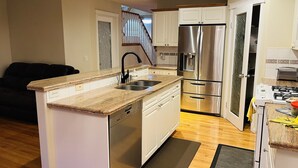 A compact kitchen with white cabinets, a stainless steel refrigerator, and a built-in dishwasher. - Cozy house-3Bedrm-Aircon-2 Free parking-inner city (Calgary)