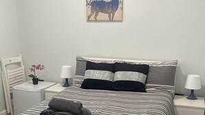 A neatly arranged bedroom with a striped bed, two bedside tables with lamps, a wall-mounted painting of a deer, and a small potted plant. - Acton Vale hotel  (London)