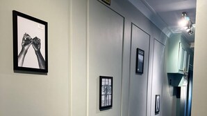 A hallway with framed artwork on the walls, a CCTV warning sign, and a door leading to a room with teal cabinets. - Acton Vale hotel  (London)