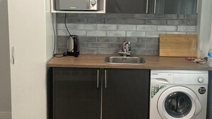 A compact kitchen with a refrigerator, microwave, sink, and washing machine. - Acton Vale hotel  (London)