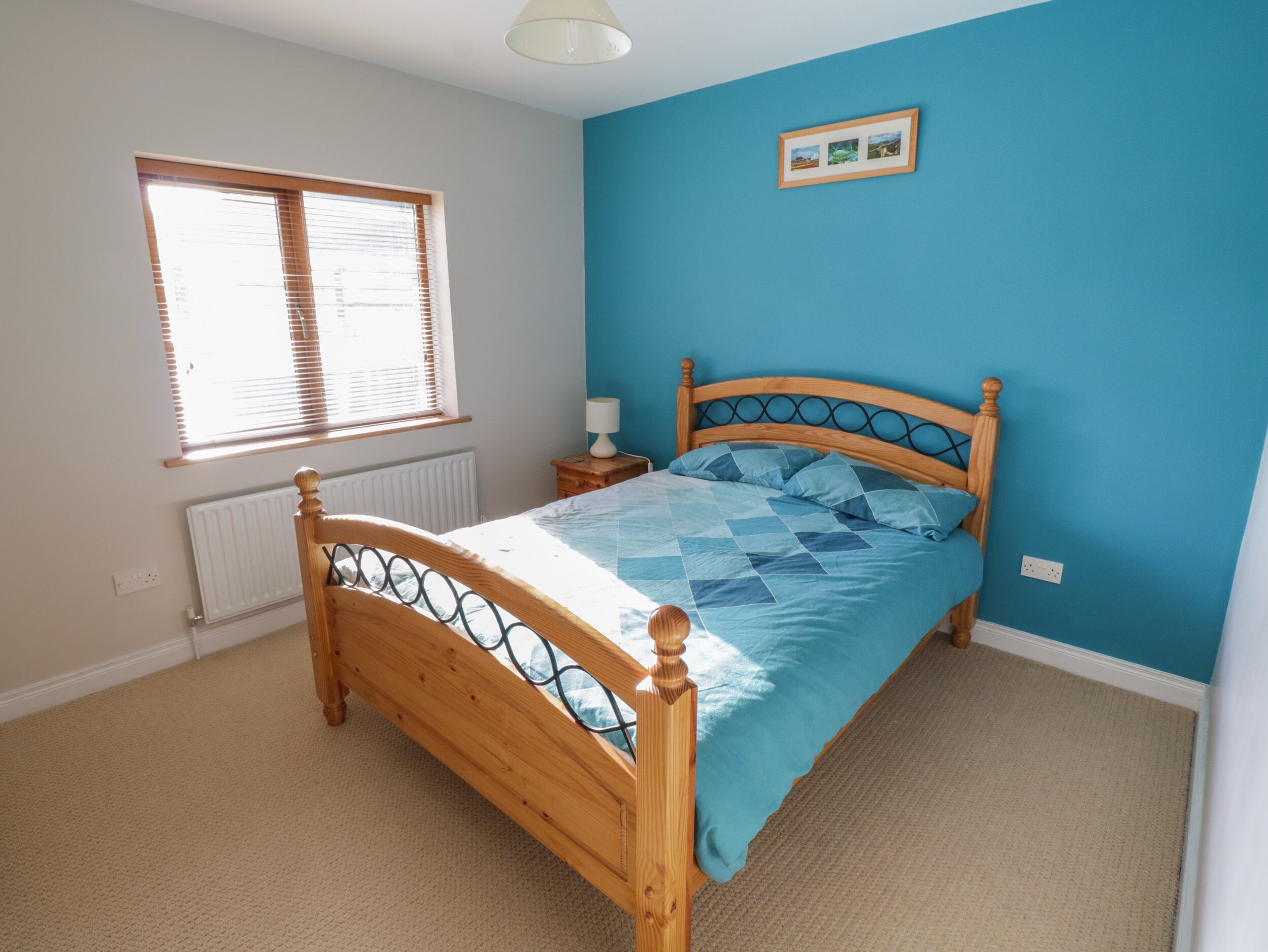 A bedroom with a wooden bed, a window with blinds, a radiator, and a picture on the wall.
