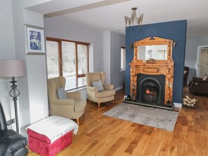 A living room with a fireplace, two armchairs, a red ottoman, and a lamp.