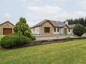 A two-story stone house with a garage, a well-maintained lawn, and a large coniferous tree in the front yard.