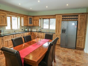 A kitchen with wooden cabinets, a stainless steel refrigerator, a dining table with chairs, and a red placemat.