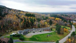 Un chalet doté d’un grand parking, entouré d’arbres aux couleurs automnales et offrant une vue sur une route sinueuse.