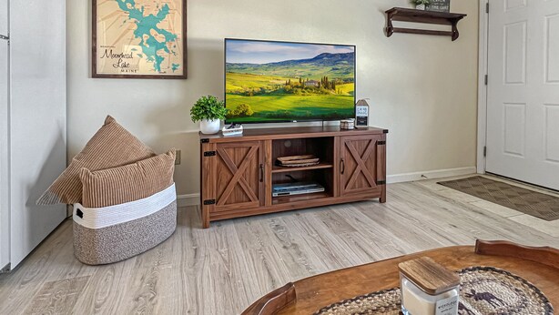 Un salon avec un meuble de rangement en bois pour l’équipement audiovisuel, un téléviseur, une carte accrochée au mur, un panier rempli de coussins et un set de table en fibres tressées posé sur une table basse.