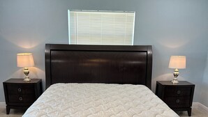 A bedroom with a large bed, two bedside tables with lamps, and a window with blinds.