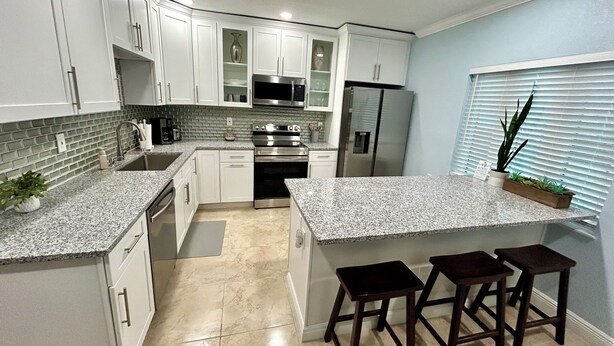 A modern kitchen with white cabinets, granite countertops, stainless steel appliances, and a central island with stools.