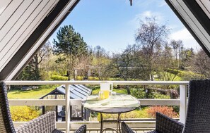 A balcony with wicker chairs and a table, overlooking a garden with trees and a house. - 3 bedroom stunning home in Rudkøbing (Rudkøbing)