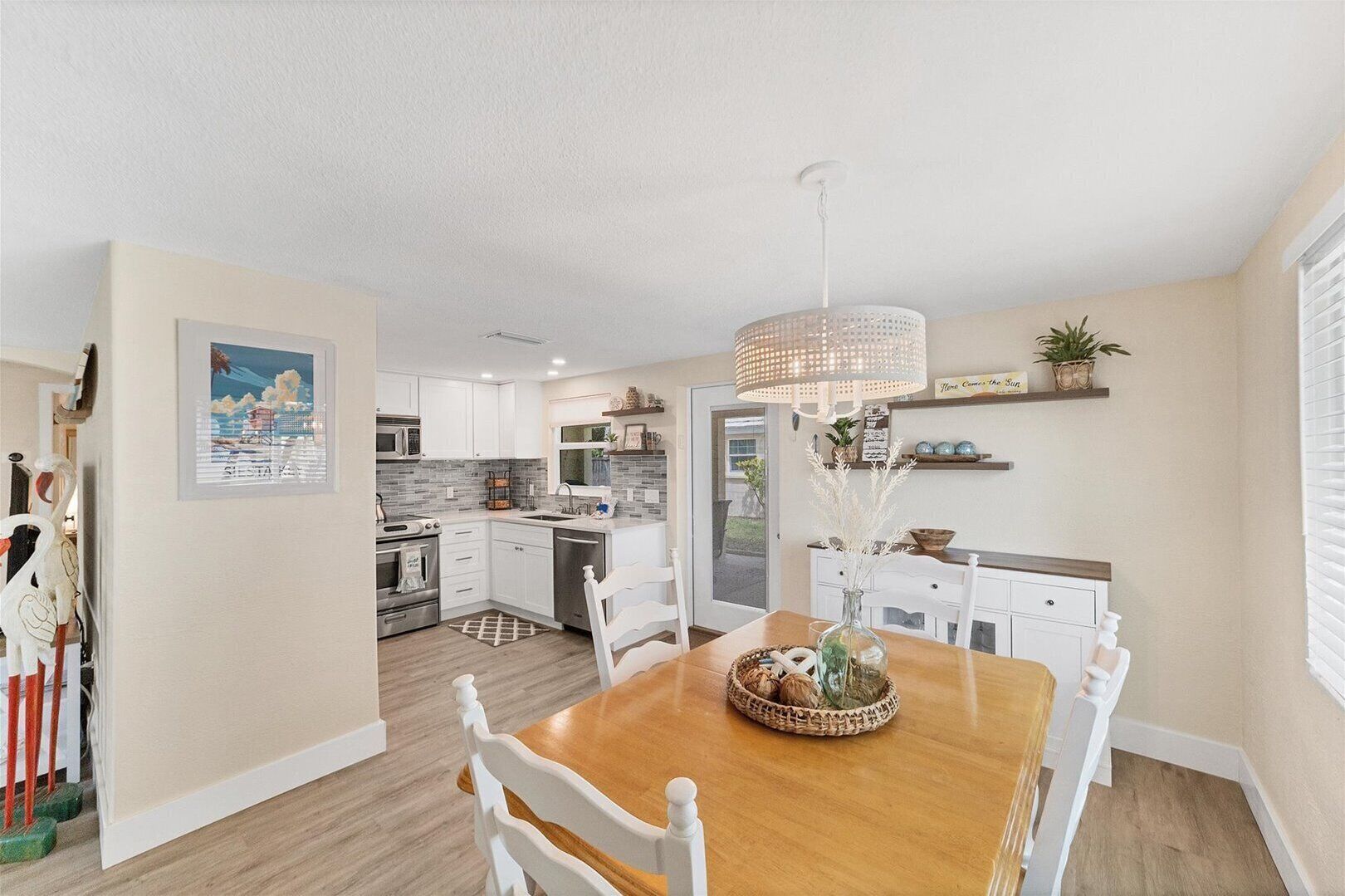 A modern kitchen with white cabinets, a wooden dining table, and a hanging light fixture.