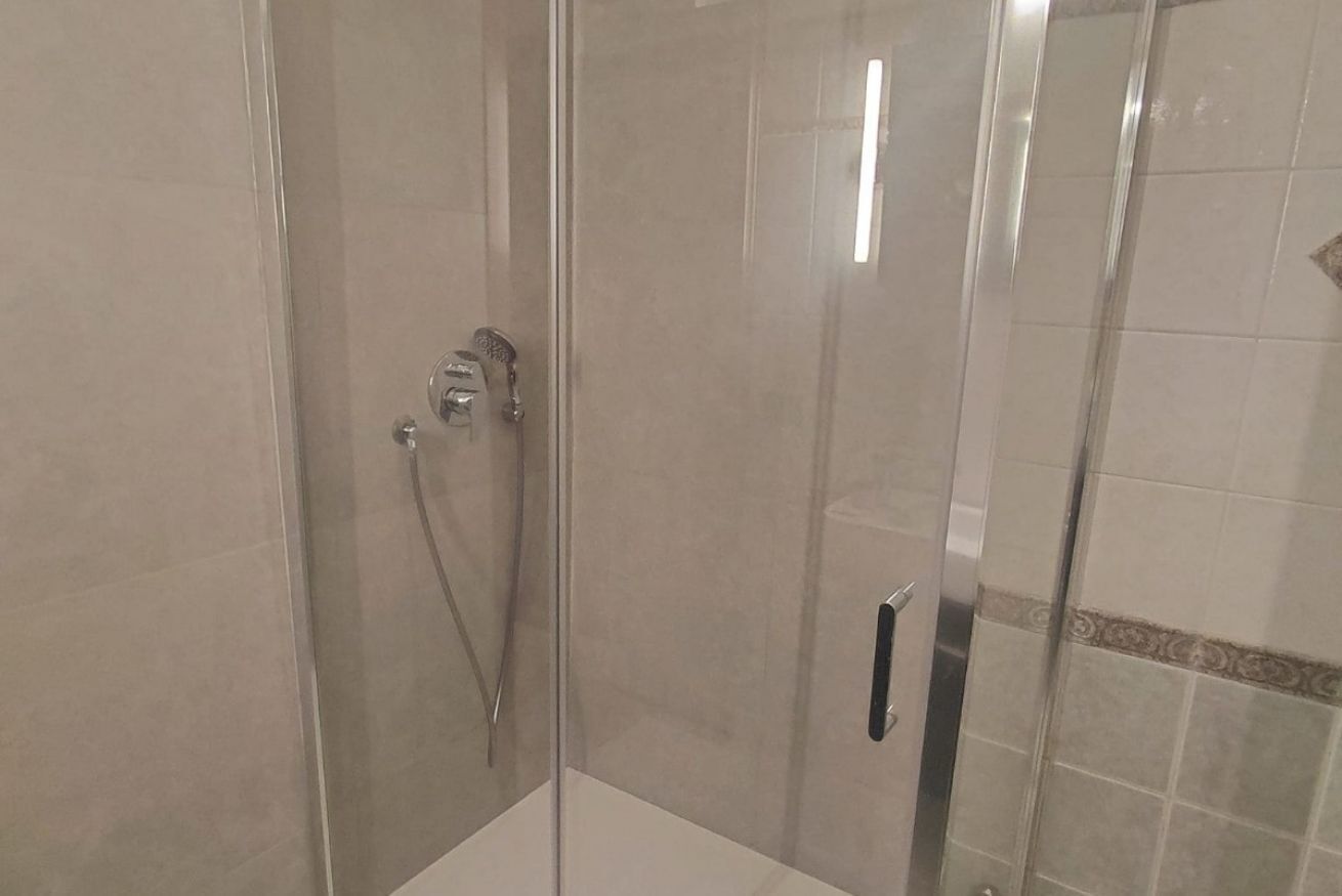 Zona d'aigua amb dutxera tancada per vidre, amb aixeta de mà i un grifer fixat a la paret.