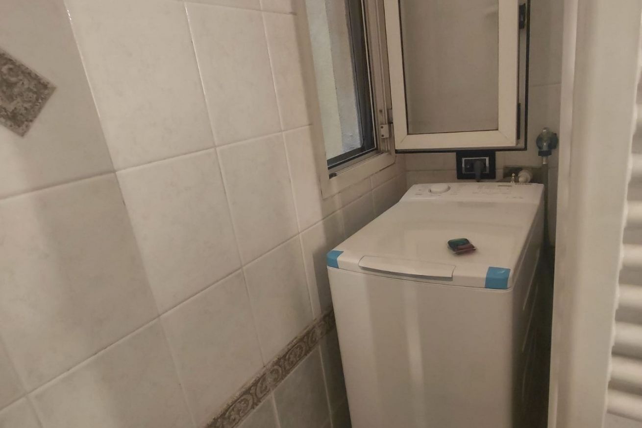 A compact bathroom with white tiles, a window, a mirror, and a white washing machine.