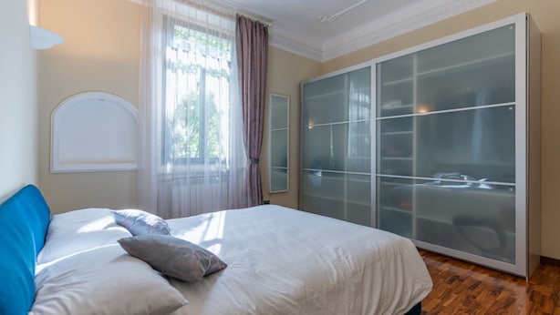 A bedroom with a bed, a wardrobe, and a window with curtains. - GuestHost - The apartment, a welcoming residence of approximately 70 square meters, is ideal for hosting up to 4 people. Located on the first floor of a building with elevator in the Washington district, one of the most elegant residential areas of Milan (Milano)