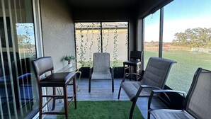En balkon med udsigt over en græsmark, to stole, et lille bord med en plante og et glasgelænder.