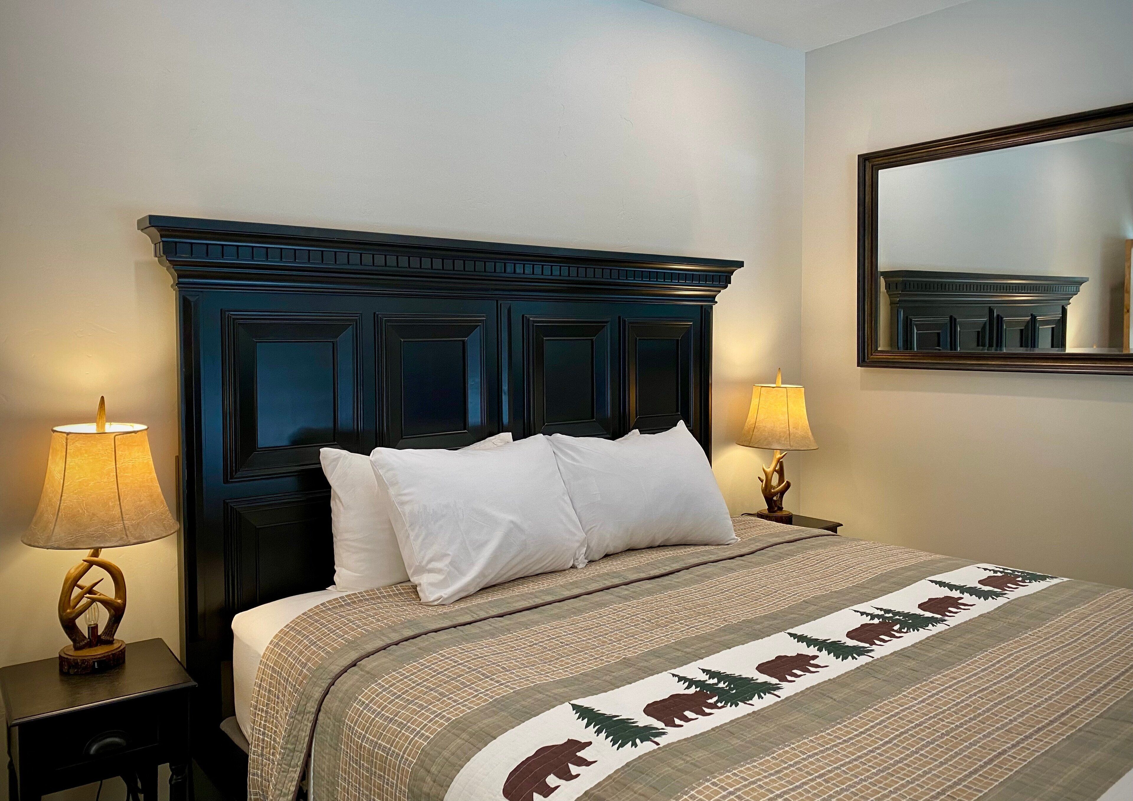 A neatly made bed with a patterned bedspread, two bedside lamps, and a dark wooden headboard.