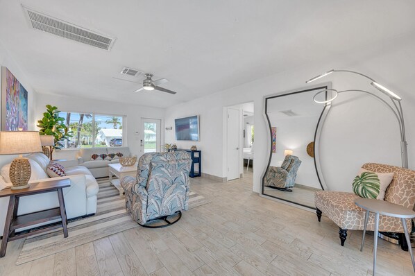 A spacious living room with a ceiling fan, a large mirror, and a modern floor lamp.