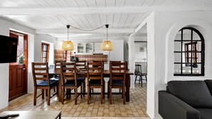 A dining area with a wooden table and chairs, two hanging lamps, and a kitchen in the background. - 4 bedroom awesome home in Rudkøbing (Rudkøbing)