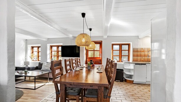 A spacious dining area with a long wooden table and chairs, a television mounted on the wall, and a kitchen in the background. - 4 bedroom awesome home in Rudkøbing (Rudkøbing)