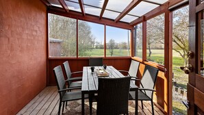 A covered patio with a table and chairs, large windows, and a view of a grassy area. - 4 bedroom awesome home in Rudkøbing (Rudkøbing)