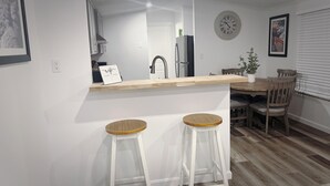 A modern kitchen with white cabinets, a wooden countertop, and two wooden stools.