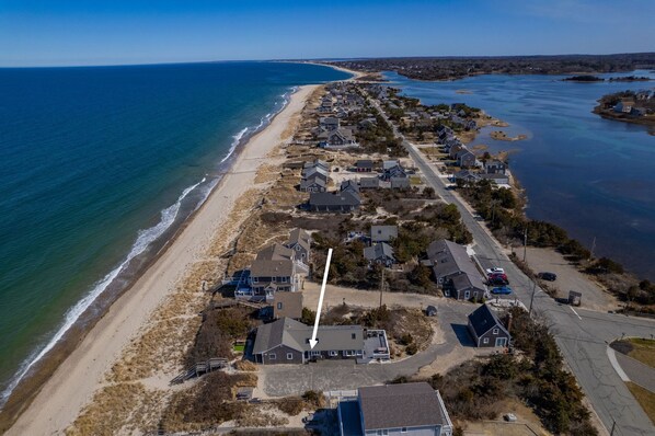 An aerial view of a coastal residential area with houses along the beach and a road leading to the water.