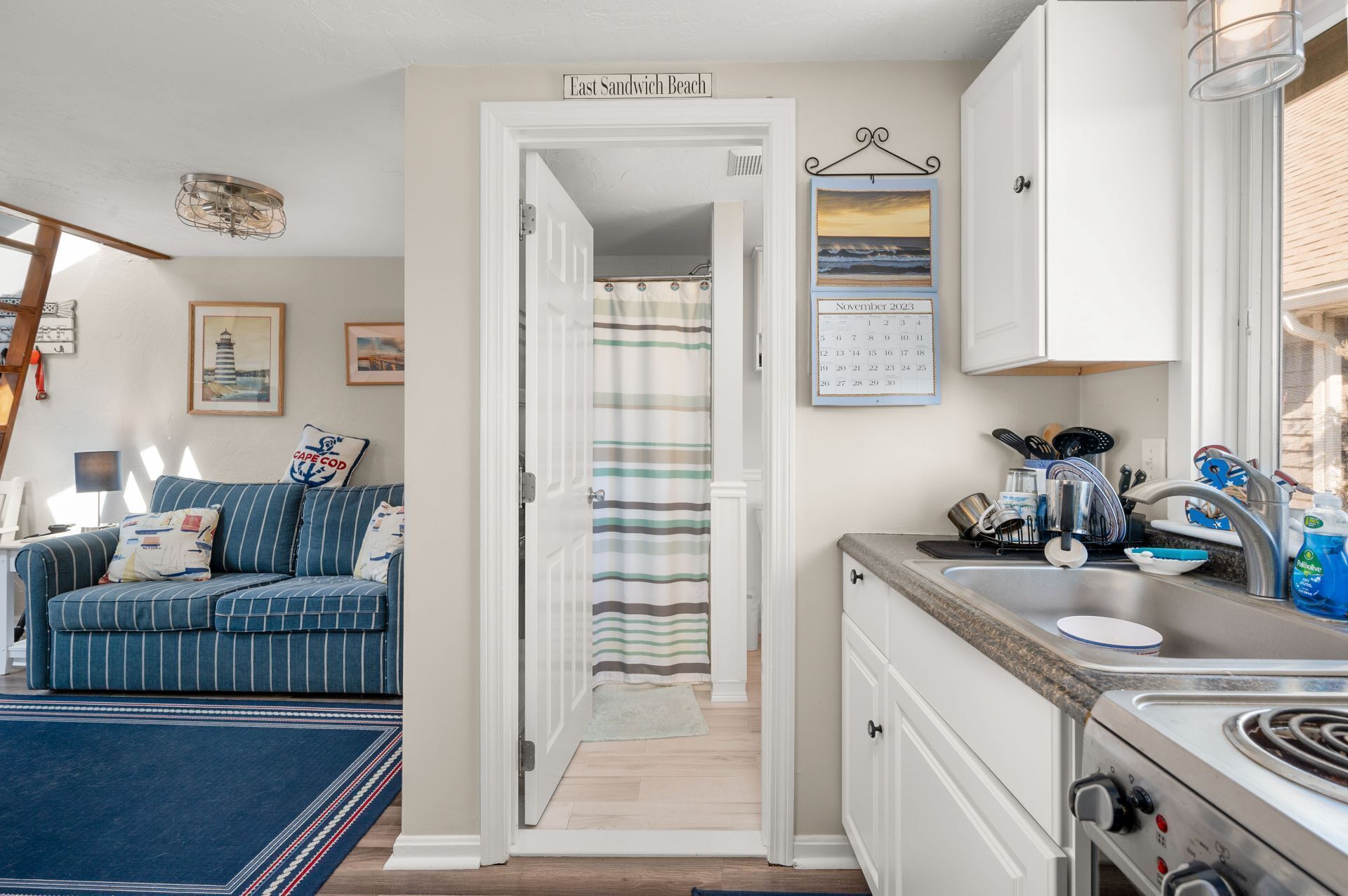 A cozy living room with a striped sofa, a dining area with a striped tablecloth, and a kitchen with a stove and cabinets.