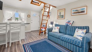 Un salón acogedor con un sofá azul a rayas, una escalera de madera y almohadas con motivos náuticos.