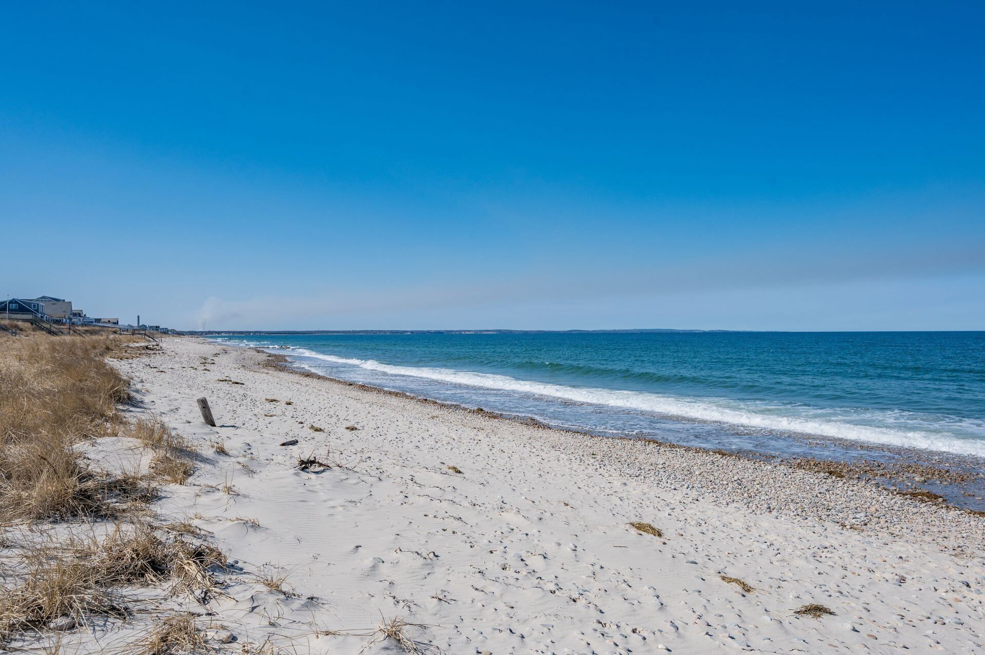 Una playa con cielo despejado, orilla de arena y algunos edificios a lo lejos.