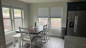 A kitchen with a dining table, chairs, a refrigerator, and large windows. - Family home (Roseburg)