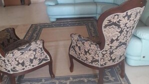 Un salon avec un canapé bleu clair, deux fauteuils à motifs, un meuble en bois et un tapis à motifs.