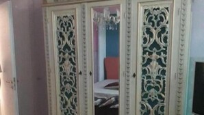 Une pièce comprenant une grande armoire richement décorée avec des portes miroir, un lit avec une tête de lit rouge et une petite table sur laquelle se trouve un téléviseur.
