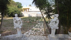 Un chemin de jardin dallé de pierres, bordé de deux statues blanches.