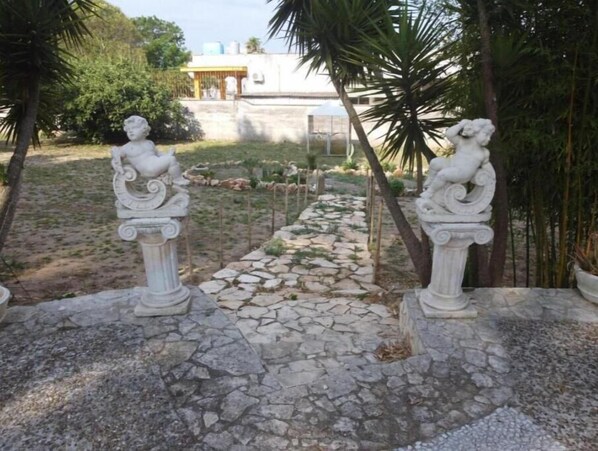A garden pathway with stone paving, flanked by two white statues. - Pink villa (Latiano)