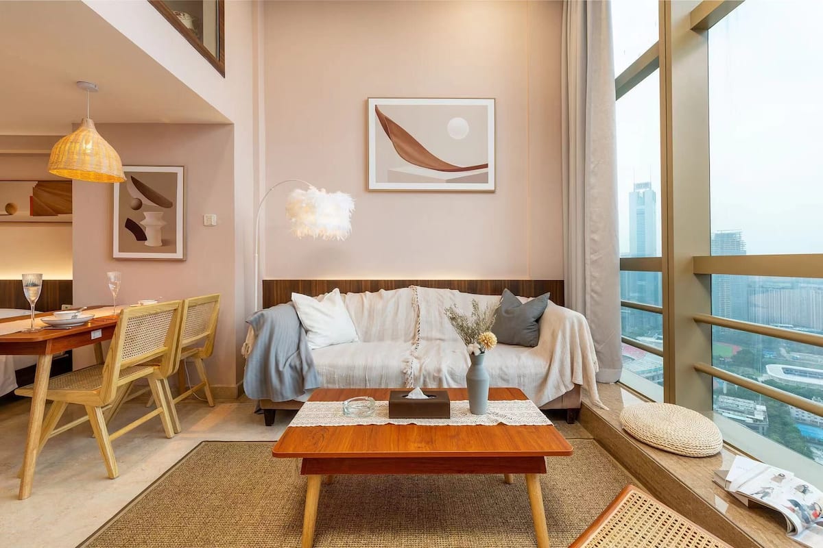 A modern living room with a sofa, a dining table with chairs, a coffee table, and a large window with a city view.