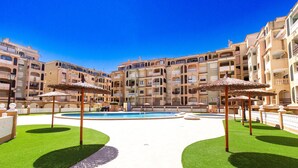 A hotel courtyard with a swimming pool, multiple balconies, and outdoor umbrellas. - Cozy apartment in Torrevieja (Torrevieja)