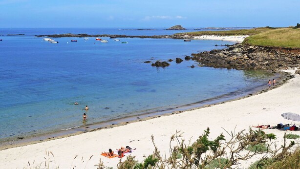 Une plage avec une eau d’un bleu limpide, un rivage rocheux et des bateaux.