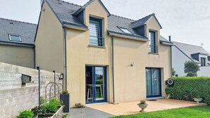 Une maison à deux étages avec un toit en pente, une porte d’entrée et un petit jardin devant, agrémenté d’une clôture en bois et d’un jardinier.