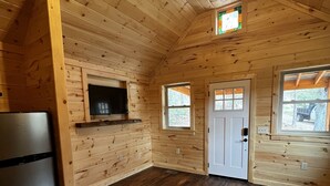 Interior de una cabaña de madera con ventilador de techo, televisor integrado y refrigerador.