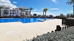 A swimming pool with a clear blue sky, palm trees, and a building in the background. - Lovley Ground Floor 2 Bed with direct access to the Pool, Free WiFi (Sucina)