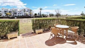 A patio with a table and chairs, a small planter, and a view of a residential area with houses and a hedge. - Lovley Ground Floor 2 Bed with direct access to the Pool, Free WiFi (Sucina)
