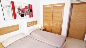 A bedroom with a bed, a nightstand, a wooden wardrobe, and a wall-mounted air conditioning unit.