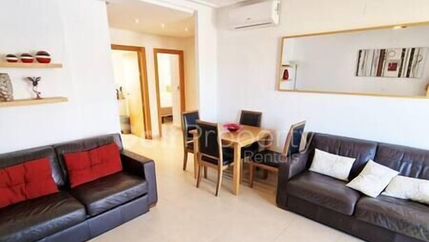 A living room with two dark sofas, one with red cushions, a wooden dining table with chairs, and a large mirror on the wall.