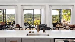 A modern kitchen with a large island, white cabinetry, and a view of a lush landscape.
